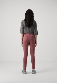 Grijze korte mouwen top in combinatie met aansluitende roze leggings, met een elastische tailleband en achterzakken. Model draagt grijze sport schoenen.