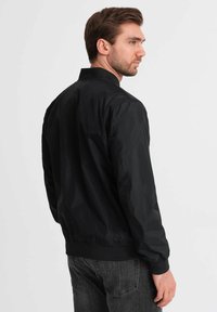 Veste bomber noire en tissu léger et lisse. Dotée d'un col montant, de poignets et d'un ourlet élastiques ; conçue avec une coupe décontractée.