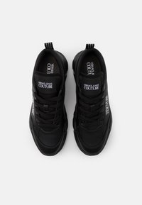 Zapatillas negras de cuero con un diseño elegante. Características incluyen cordones, un collar acolchado y logotipos en la lengüeta y el costado.