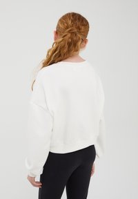 Felpa bianca, oversize, con spalle scese e polsini larghi, abbinata a leggings neri; texture morbida e vestibilità rilassata.