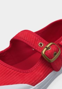 Κόκκινο παπούτσι Mary Jane από κορντουρό με λουρί και αγκράφα από ορείχαλκο και λευκή λαστιχένια σόλα, σε γωνία που δείχνει λεπτομέρειες από πάνω και από το πλάι.