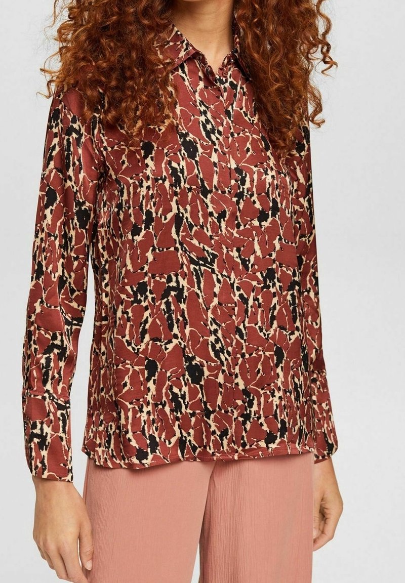 Long-sleeve blouse in rust with abstract black and cream pattern. Made from smooth fabric; features a collared neckline and button closures.