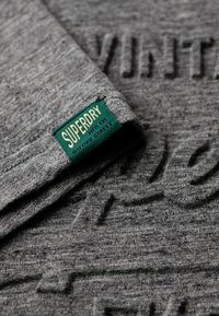 Grå bomulds T-shirt med hævet tekstdesign, ikke-branded grøn label i kanten, tekstureret stof med et afslappet look.