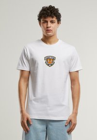 Balta medvilnė marškinėliai su išsikėlusią apvalia logotipu, kuriame pavaizduotas tigro vaizdas ir „DETROIT“ tekstas juoda ir oranžine spalvomis, trumpomis rankovėmis, standartinio kirpimo.