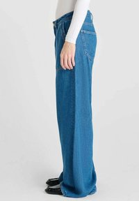 Jeans de denim azul claro con un corte recto y holgado. Presentan una cintura alta, dos bolsillos traseros y una textura suave.