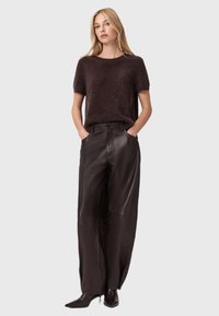 Brūns pūkains īsām piedurknēm svīteris apvienots ar augsta vidukļa melnām ādas plati kājām. Modelis valkā melnas norādītas kurpes.