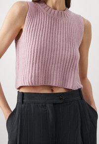 Lichtroze gebreide crop top met geribbelde textuur en een hoge ronde halslijn, gecombineerd met donkergrijze pinstriped broek met een voorste knop.