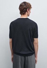 Black knit short-sleeve sweater with a relaxed fit, ribbed collar, and cuffs, worn with gray trousers. The texture appears smooth and soft.
