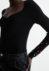 Body noir côtelé avec encolure carrée, manches longues ornées de détails décoratifs colorés, et silhouette ajustée.