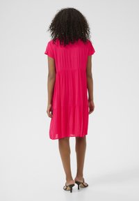 Fuchsia short-sleeve dress with a tiered design, featuring a relaxed fit and flowing fabric. Worn with black open-toe heels.
