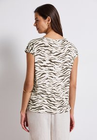 Short-sleeve, lightweight top in off-white with a green tiger stripe pattern. Soft texture, rounded neckline, and relaxed fit.
