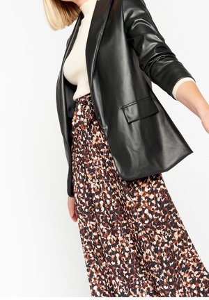 Kvinde iført en beige ribbet top, sort blazer i kunstlæder og et højtaljet, flerfarvet abstrakt mønstret nederdel.