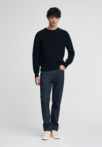 Zwarte ribgebreide trui gecombineerd met donkere spijkerbroek en lichtgekleurde sneakers. Eenvoudig ontwerp, ronde halslijn, relaxte pasvorm.