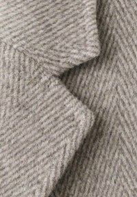 Visgraatmotief stof in lichtgrijs, een textuurrijke wolmix met zachte vezels, met diagonale strepen en een gevouwen rand.