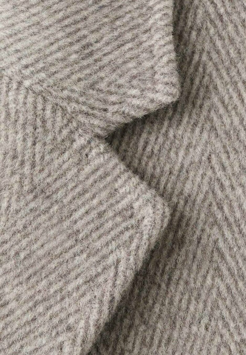 Fischgrätmuster-Stoff in hellgrau, strukturierter Wollmischung mit weichen Fasern, zeigt diagonale Streifen und eine gefaltete Kante.