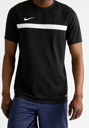 Homme portant un t-shirt Nike noir à manches courtes avec une bande blanche sur la poitrine et un short de sport bleu.