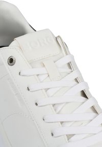 Λευκά δερμάτινα αθλητικά παπούτσια με επίπεδες λευκές κορδόνες, ανάγλυφο λογότυπο στην γλώσσα και κυκλικό μεταλλικό διακοσμητικό στο πλάι. Λείο υφή.