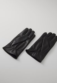 Guantes de cuero negro con una textura suave, diseño ajustado y detalles de muñeca fruncidos, con un parche de tela adicional en la parte posterior.