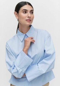 Jasnoniebieska koszula z długim rękawem i klapami, o luźnym kroju. Gładki materiał o miękkiej fakturze.