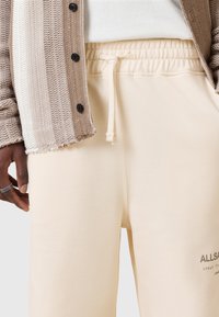 Pantaloni jogger color crema con vita elastica, dettaglio con coulisse e stampa del logo. Abbinati a un cardigan a righe texturizzato con bottoni.