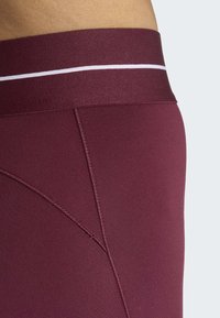 Pantalones cortos deportivos granate con una cinturilla ancha que presenta una franja blanca. Textura lisa con costuras reforzadas y un diseño ajustado.