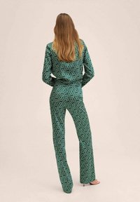 Combinaison verte à motifs avec un design en chaîne, manches longues et pantalons évasés, dotée d'une taille ceinturée et d'une texture de tissu lisse.