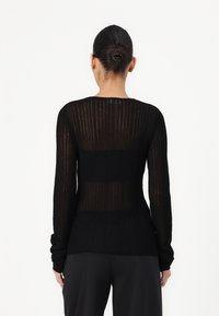 Maglione lungo nero a maniche lunghe, con un design trasparente e una silhouette aderente, caratterizzato da una texture morbida e un colletto rotondo.