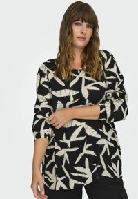 Blusa en blanco y negro con un audaz patrón de hojas, tejido suave, mangas largas con detalles fruncidos y un corte relajado.