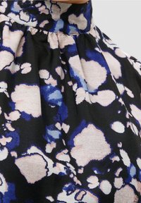 Svart tygtop med hög hals, plisserad design och abstrakta blå och rosa sprutmönster. Slät textur med mjuk fall.