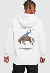 Weißer Hoodie mit einer detaillierten Illustration eines Cowboys auf einem braunen Pferd, mit dem Text "LEBE IM MOMENT" unter dem Design.