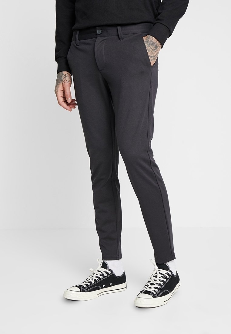 Ciemnoszare slim-fit spodnie, wykonane z gładkiego materiału, z przednimi kieszeniami, zapięciem na guzik oraz tapered leg design. Noszone z czarnymi trampkami.