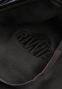 Unutrašnjost od crne tkanine s izvezenim logotipom "RIVRA". Mekana tekstura sa glatkim završetkom i kontrastnim šavovima blizu patentnog zatvarača.