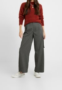 Rode fluffy trui met lange mouwen, gecombineerd met grijze wijde broek met een zijzak, afgemaakt met witte sneakers.