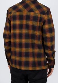 Camisa de cuadros con colores naranja, amarillo y negro, con cuello abotonado, mangas largas y dobladillo recto. Textura de la tela visible.