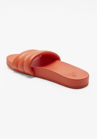 Orange hæl sandaler med en bred, polstret, struktureret rem og en flad, solid sål. Materialet ser glat og let skinnende ud.