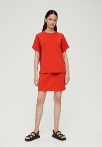 Rode katoenen sweatshirt- en rokken set met verhoogd bladdesign, korteblousjes en een relaxte pasvorm, gecombineerd met zwarte sandalen met bandjes.