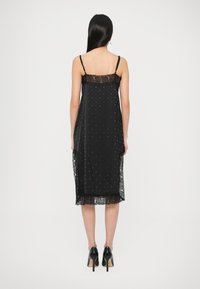 Fekete slip ruha csipkés szegéllyel, állítható spaghetti pántokkal és pöttyös mintával, középmálig érő, áttetsző csipke részletekkel az alján.