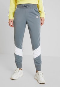 Grå träningsbyxor med elastisk midja, med vita sidopaneler och en liten Nike-logotyp på låret. Tillverkade av ett mjukt, elastiskt material.