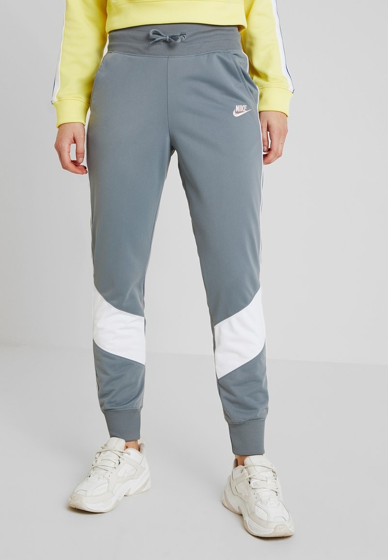 Grå träningsbyxor med elastisk midja, med vita sidopaneler och en liten Nike-logotyp på låret. Tillverkade av ett mjukt, elastiskt material.