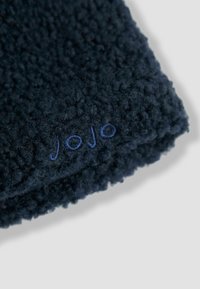 Bufanda de forro polar azul marino con una superficie texturizada y esponjosa. Presenta el bordado "jojo" en un azul claro en contraste. Forma rectangular.