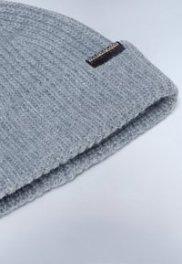Šedá pletená čepice s ohrnutým lemem, na kterém se nachází černá nálepka s názvem značky. Texturovaný materiál s žebrovaným vzorem.
