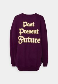 Sweat-shirt violet foncé avec texte jaune et blanc indiquant « Past Present Future » au dos, présenté sur un fond uni clair.
