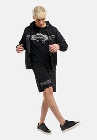 Black zip-up hoodie, graphic black t-shirt with white print, black shorts with logo, black sneakers with white soles. Smooth texture.