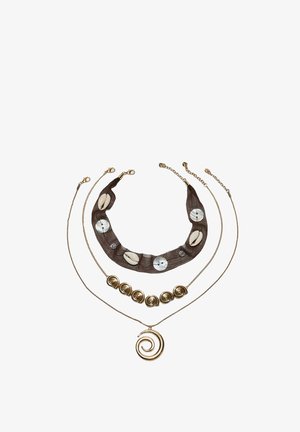 Trois colliers superposés : le haut avec un tissu foncé, des coquillages et des accents ronds ; le milieu avec des perles en spirale dorées ; le bas avec un pendentif en spirale doré.