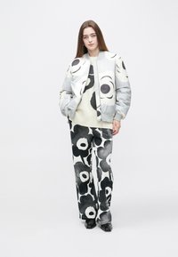 Szara kurtka bomberka z dużym czarno-białym kwiatowym nadrukiem, kremowy sweter i czarno-białe wzorzyste spodnie o szerokich nogawkach. Czarne buty.
