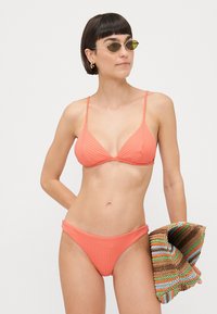 Coral ribbed bikini top with triangle cups and adjustable straps, paired with matching high-waisted bikini bottom. Textured, lightweight fabric.