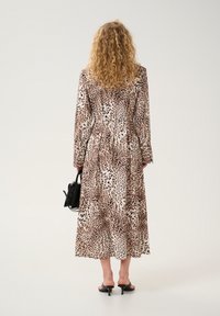 Abito lungo con stampa leopardata, vita segnato, maniche lunghe e gonna fluida, abbinato a sandali neri con cinturini e una piccola borsa nera.