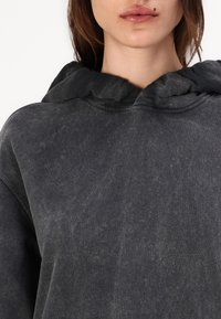 Dark grey hooded sweatshirt featuring a soft, textured fabric with a slight distressed finish and ribbed trim around the neck and hood.