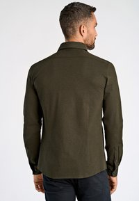 Donkergroen langemouwen shirt met een gestructureerde kraag, getailleerde pasvorm en knoopmanchetten. Gladde stofstructuur met minimale details.