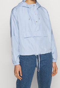 Vaaleansininen, kevyt huppari, jossa on edessä nepparit, kiristysnyöri vyötäröllä ja elastiset hihansuut. Yksinkertainen muotoilu ilman näkyviä kuvioita.